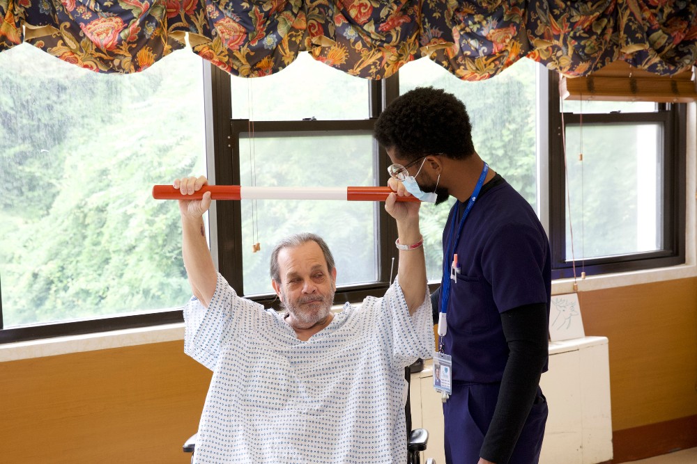 Therapist helping elderly man with yoga for tight muscles.