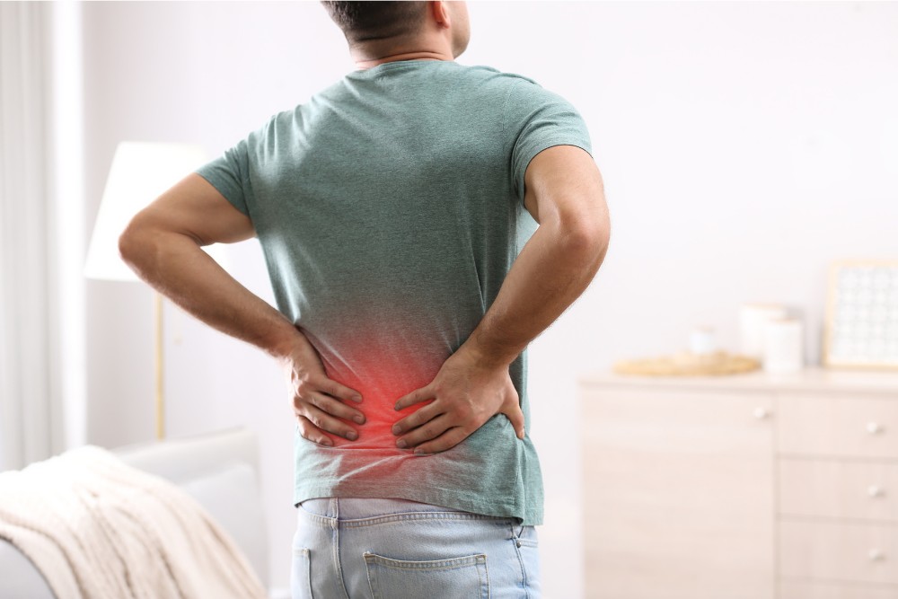 Man experiencing lower back pain, holding his back with a highlighted red area, indicating spinal arthritis.